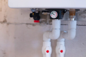 Close-up of plumbing components including valves and a pressure gauge. The pipes are white plastic, mounted on a concrete wall.