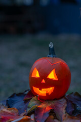 Jack o' lantern pumpkin glowing with light on autumn leaves