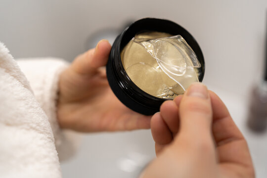 Womans hand takes golden hydrogel eye patch from jar. Skincare and reducing wrinkles