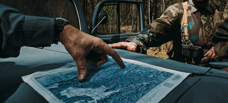 German Army officers looking at a topographic map to plan a route. Hands pointing at a location on paper placed on a car hood. Historical reconstruction of the Wehrmacht operations.