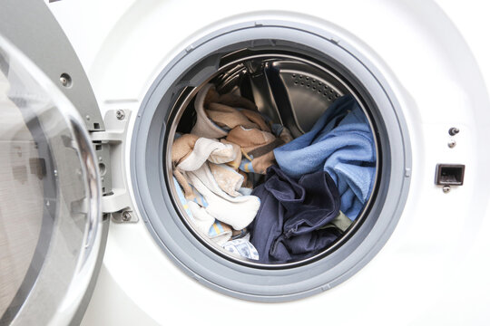 Front loading washing machine with clothes inside drum. Open washing machine door showing laundry before wash cycle. Household appliance for home laundry cleaning and fabric care concept.
