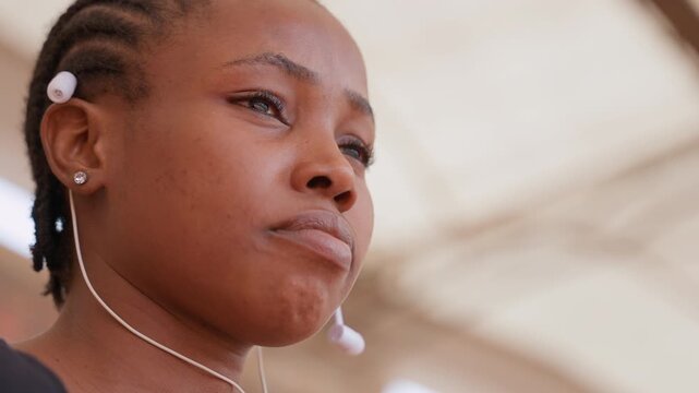 black woman in stadium focused gaze frames suggest competitor, trainee, leader, contender roles, braided hair with earbuds, closeup profile revealing steady jaw and attentive eyes, pre competition