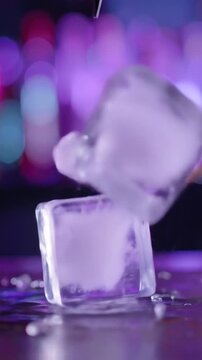 Close-up of a large ice cube being pierced with a l bar, creating a splash.