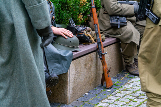 Historical reenactment: WWII soldiers with Mauser rifle, Stahlhelm helmet, and military gear resting on a bench during a living history event.