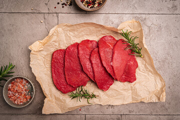 Raw sliced beef or lamb tenderloin meat, beef steaks on paper with spices for cooking on gray background, top view © petrrgoskov