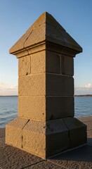 Fototapeta premium Stone pier structure by tranquil coastal waters under clear blue sky at sunset