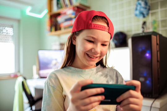 Smiling preteen girl playing mobile game in bedroom