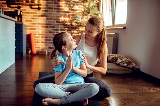 Mother and daughter meditating on a yoga mat at home