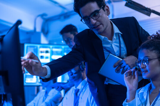 Project manager pointing at computer screen to explain and help team solve software issues in at security operations center. Diverse IT specialists collaborating on systems in the office.
