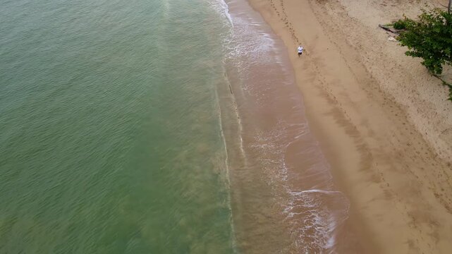 A couple walking on a tropical sandy beach in Sri Lanka, a drone view of people walking on the beach. A man and a woman in a white dress walking on an empty beach in Sri Lanka.