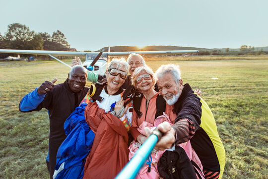Senior friends taking skydiving selfie at sunset airfield