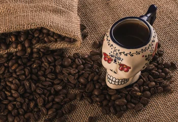 Fototapete Rund Cafe Detail of Espresso coffee served in a cup shaped like a sugar skull from the Day of the Dead, accompanied by coffee beans coming out of the sack, on a wooden table  © Marco