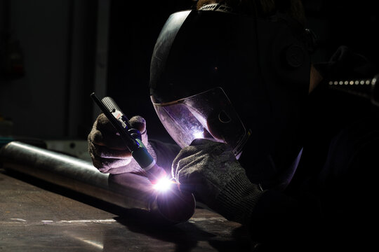 Worker performs TIG welding on metal with tungsten electrode and argon gas