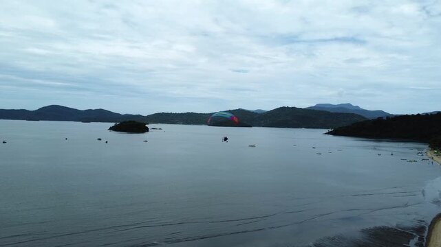 Tandem paramotor turning and flying along Jabaquara Beach and over the water with a stunning view of the Paraty bay, the small islands and the mountains covered with dense forest in Paraty, Brazil
