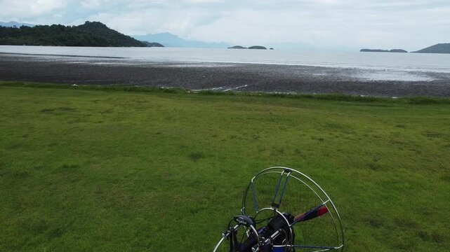 Drone shot flying over parked paramotor on the Jabaquara Beach in Paraty, with a stunning view of the Paraty bay, the small islands and the mountains covered with dense forest in Paraty, Brazil