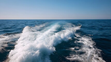Boat wake creates a trail of white foam on the vast blue ocean under a clear sky symbolizing movement and journey