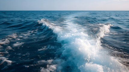 Fototapeta premium A powerful boat wake churns through the deep blue ocean leaving a trail of white foam and spray against the horizon