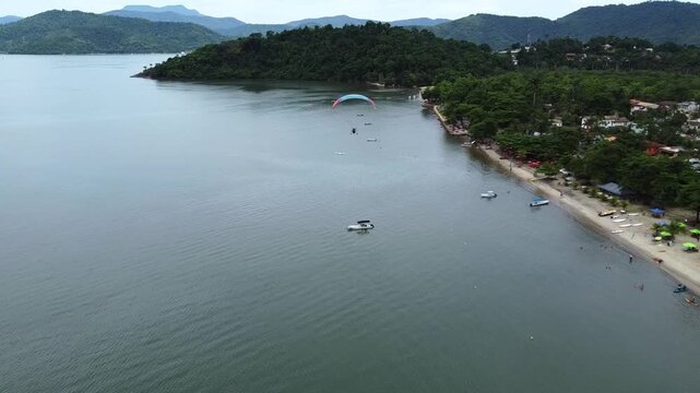 Tandem paramotor flying along Jabaquara Beach over the water with a stunning view of the Paraty bay, the small islands and the mountains covered with dense Atlantic Forest in Paraty, Brazil