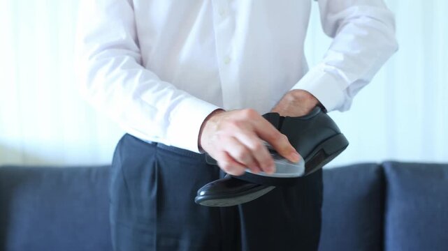A man in a white shirt and dark trousers meticulously polishes a black dress shoe, evoking care, professionalism, and the quiet dignity of daily preparation.
