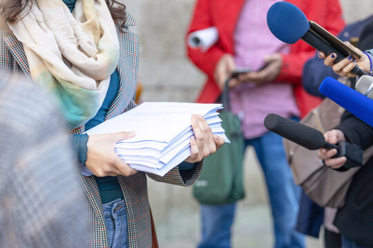 Whistleblower holding documents giving statement at press conference, speaking to journalists with microphones, concept of corruption exposure, public interest, media coverage