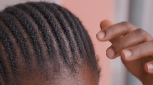 closeup black child cornrows being adjusted, mothers hand gently smoothing neat rows against soft pink wall, natural light, scalp detail, textured hair, intimate home haircare routine, protective