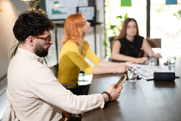 Obraz premium Business meeting in a modern office with three professionals discussing strategies while one checks their smartphone