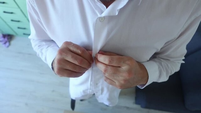 Close-up of hands carefully buttoning a crisp white shirt, highlighting precision, quiet ritual, and the dignity of daily preparation.