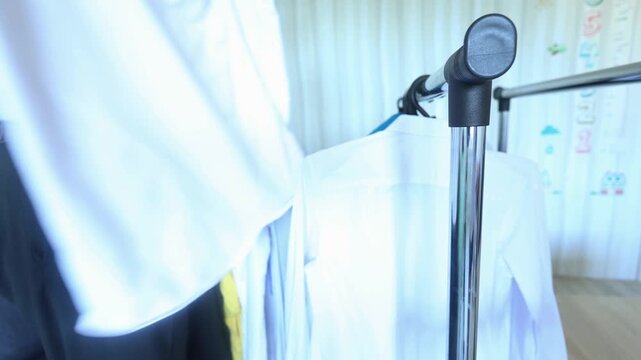 A man carefully hangs crisp white shirts on a clothing rack, emphasizing order, care, and the quiet ritual of preparing for the day with intention and dignity.