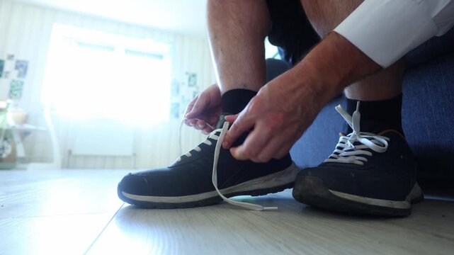 Close up of hands tying white laces on worn navy sneakers, capturing a grounded, everyday ritual of preparation, comfort, and quiet readiness.