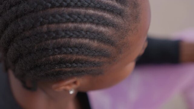 overhead view braided hair holding pen, closeup of cornrows and earring, calm study posture and concentrated expression, textured scalp detail and soft ambient light, intimate academic scene