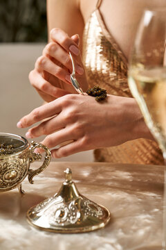 Luxury lifestyle: Woman in a gold sequin dress placing black sturgeon caviar on her hand with a silver spoon.