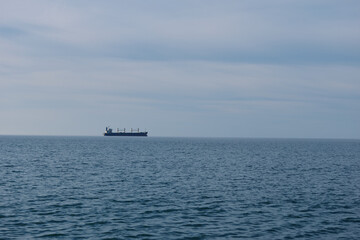 Cargo ship sailing on a calm sea with distant horizon and blue sky, a quiet maritime scene featuring a lone vessel at sea and expansive water.