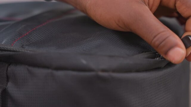 black fingers adjusting broken zipper on bag meticulous repair attempt indoors slow careful motion textured black nylon red seam tiny slider focus on fingers technique soft light patient mood