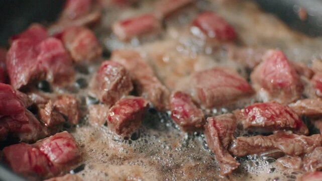Beef pieces are cooking in a pan with vegetables, creating steam and sizzle sounds