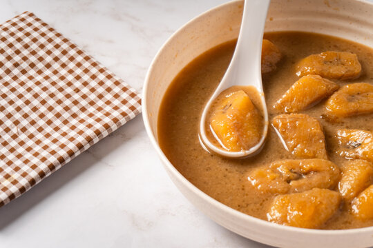 Top view of Kolak pisang on a white plate with a white spoon. Indonesian dish for breaking the fast, during Ramadan or Eid al-Fitr. Sweet soup made from bananas with coconut milk and brown sugar. 