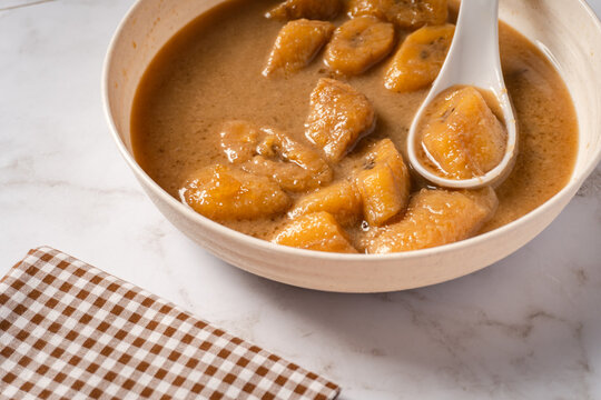 Kolak pisang on a white plate with a spoon. Popular Indonesian dish for breaking the fast, during Ramadan or Eid al-Fitr. Sweet soup made from bananas with coconut milk and brown sugar. 