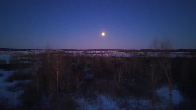 Aerial footage of a full snow moon pulling back over trees