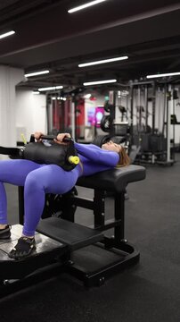 Vertical screen woman performs hip thrust exercise in gym lifting padded support with controlled movement focusing on lower body strength and stable training rhythm