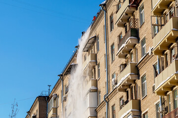 Obraz premium Communal services workers industrial climbers remove snow from the house roof in winter. Cleaning city streets, roads and building roofs after snow storm in Moscow, Russia.