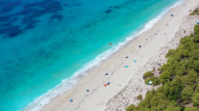 Beautiful beach in greece with very few people parasols and tents. Aerial view from above over sandy coastline and pristine water, Greek island