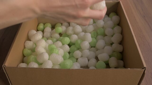 Biodegradable starch foam peanuts being tossed into a cardboard box, showcasing eco-friendly packaging materials in a clean environment. Ecofriendly packaging