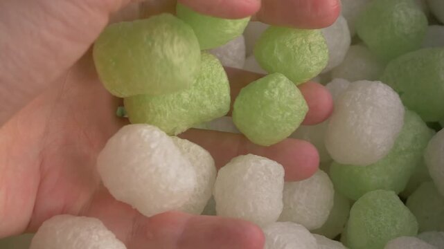 Hand reaches for biodegradable starch foam peanuts, showcasing ecofriendly packing materials in a close-up view of colorful shapes. Ecofriendly packaging