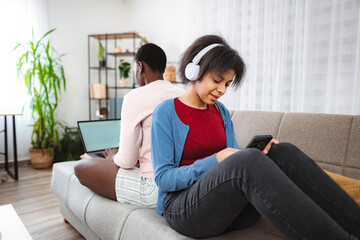 Obraz premium Teenager listening music and texting while her sister is working on laptop