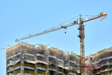 Tower crane and residential buildings under construction against blue sky.