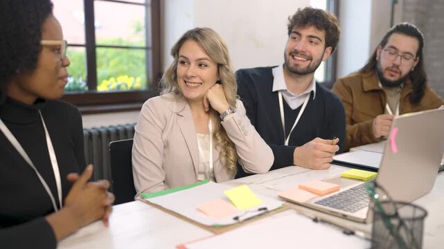 Group of young diverse colleagues sitting in a modern open-plan office and having a friendly discussion.