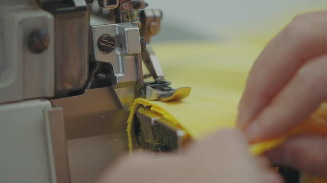 Close-up of an industrial overlock sewing machine stitching and trimming the edge of a yellow fabric.