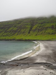 Verdant nordic landscapes of the Faroe Islands. The picturesque black sand beach under green slopes near Sandvik village, Suduroy island.