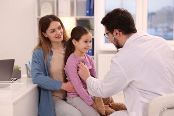 Fototapeta premium Little girl and her mother having appointment with pediatrician in hospital. Doctor checking child with stethoscope