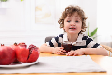 Little boy with fresh pomegranate juice at table indoors. Space for text