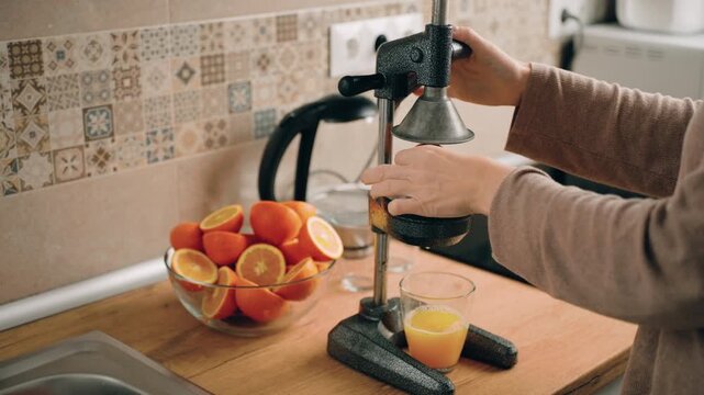 Preparing fresh orange juice in a home kitchen as part of a healthy morning. Female hands cut and squeeze oranges using a manual juicer. Calm lifestyle, natural nutrition, simple home routine.